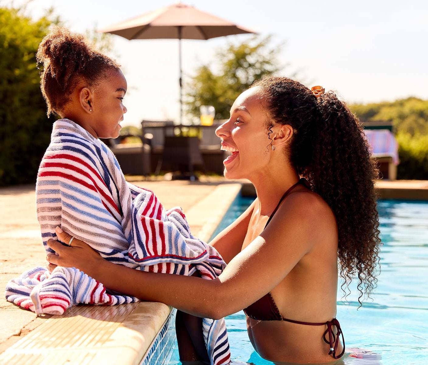A laughing woman wraps a child in a towel poolside