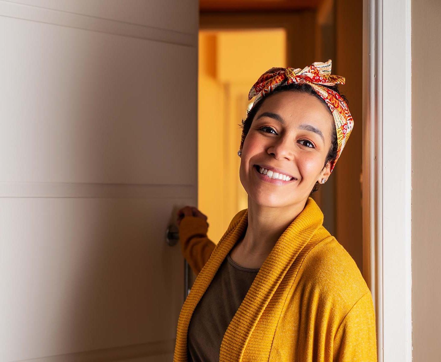 A smiling woman in a yellow headwrap and sweater.